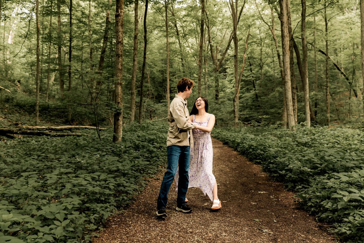 A couple embraces while dancing on a forest path surrounded by lush green foliage.