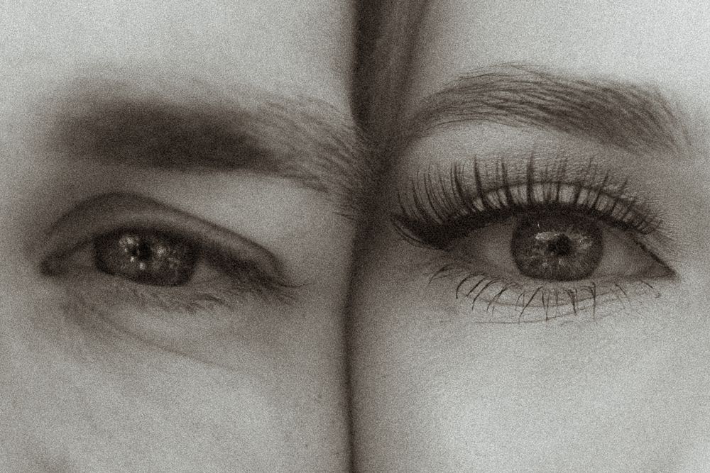 A black and white artistic close-up photograph shows two eyes with long eyelashes side by side.
