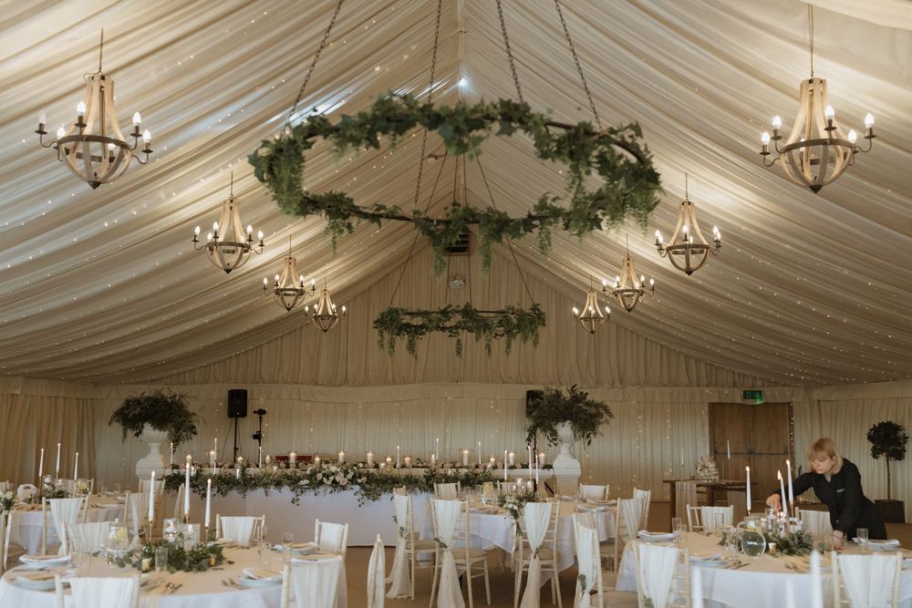 Elegant white wedding reception marquee with crystal chandeliers and draped fabric ceiling decorations create a romantic ambiance.