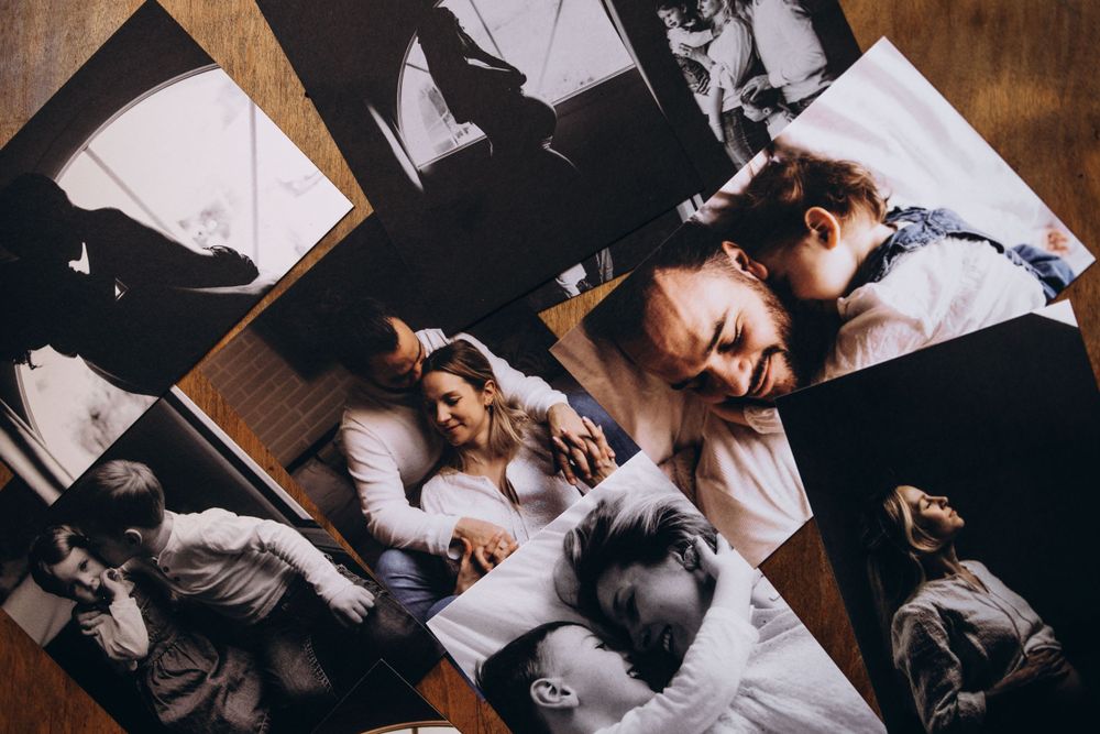 Scattered black and white photographs on wooden surface show sleeping people and dogs cuddled together in bed.