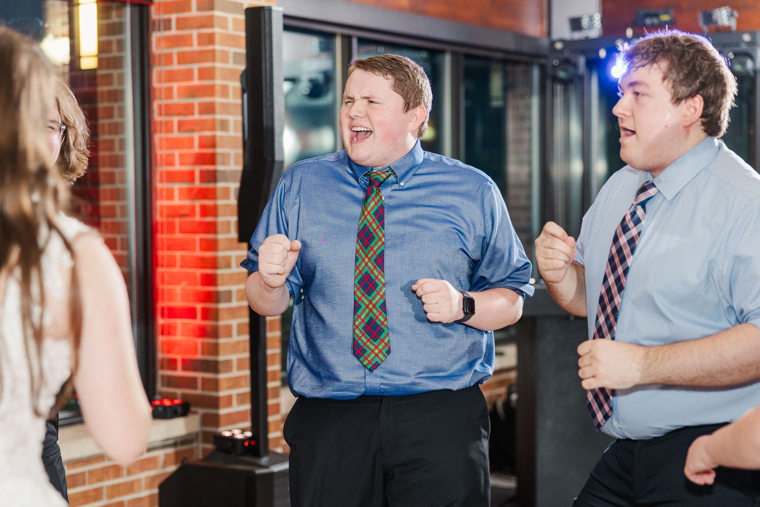 Two individuals in business attire appear animated and excited while having a conversation outside a brick building.