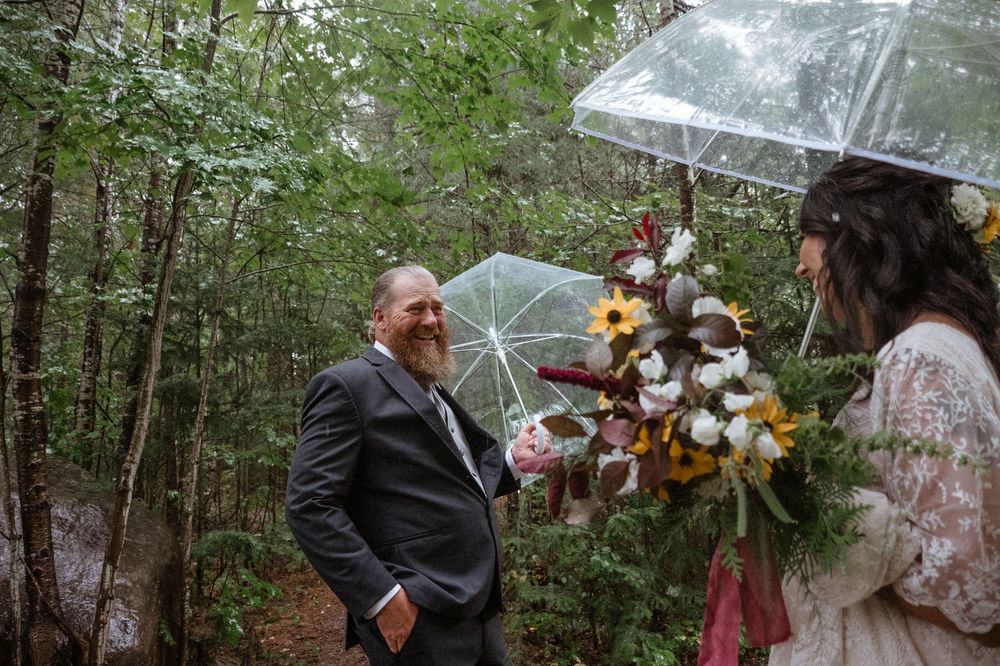 A wedding moment captured in the woods with clear umbrellas and a beautiful autumn bouquet.