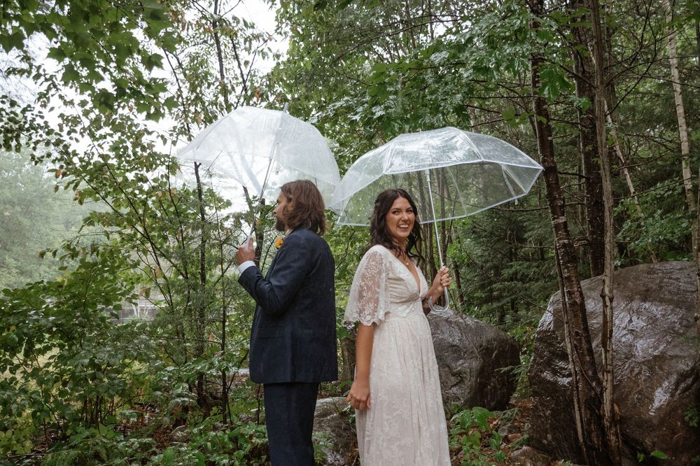 A couple shares an intimate first look moment with clear umbrellas in a lush forest setting.