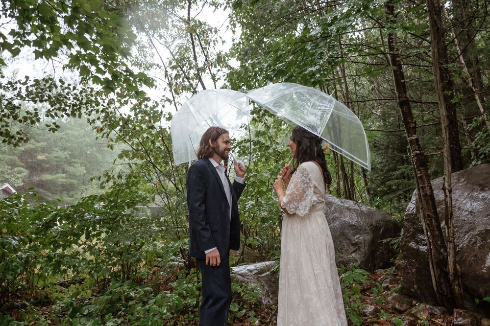 Couple sharing an intimate moment under a clear umbrella in a lush forest setting while it rains.