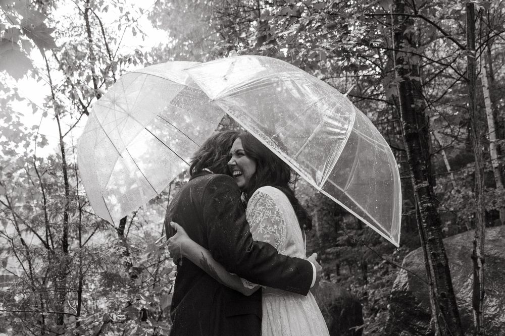 A romantic moment under a clear umbrella in a wooded forest setting captured in black and white.