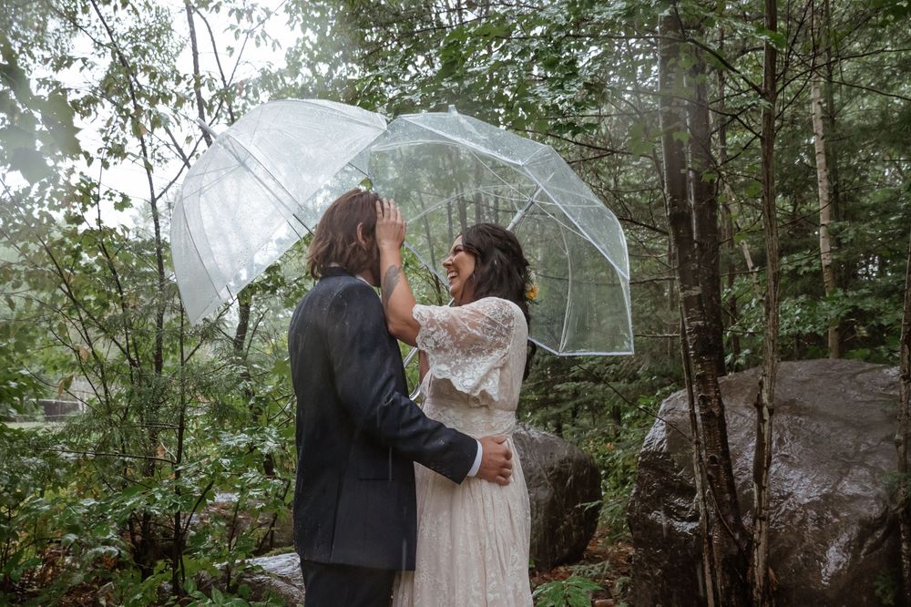 Wedding ceremony in a moody forest setting with people holding clear umbrellas on a rainy day.