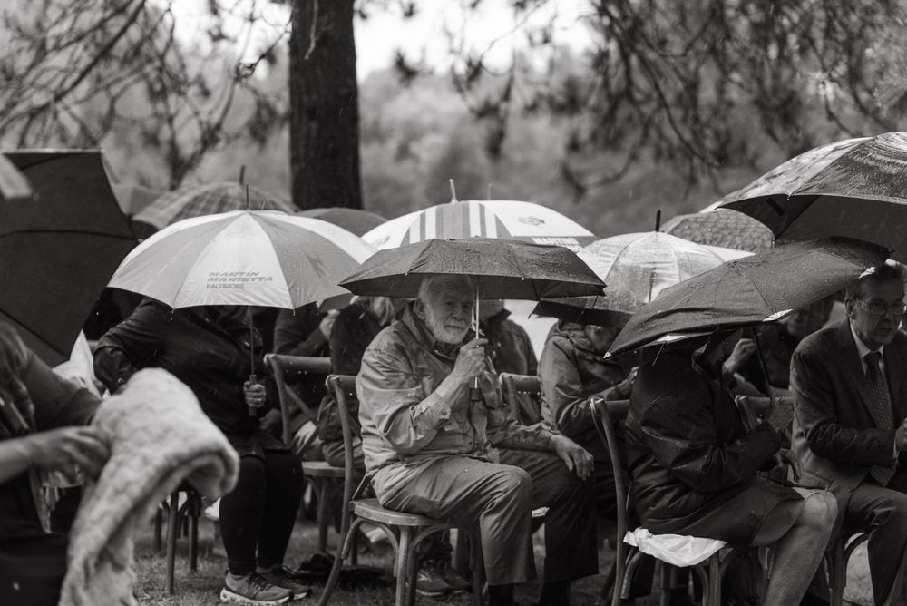 A crowd of people sit under umbrellas during a rainy outdoor event in black and white photography.