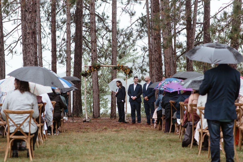 Guests seated on wooden chairs in a misty forest setting for an outdoor wedding ceremony.