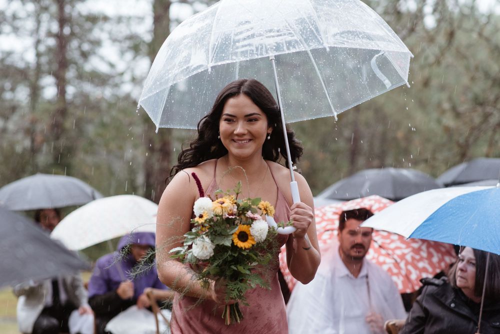 Someone holds a beautiful floral bouquet while walking under a clear umbrella at an outdoor event with other umbrellas visible.