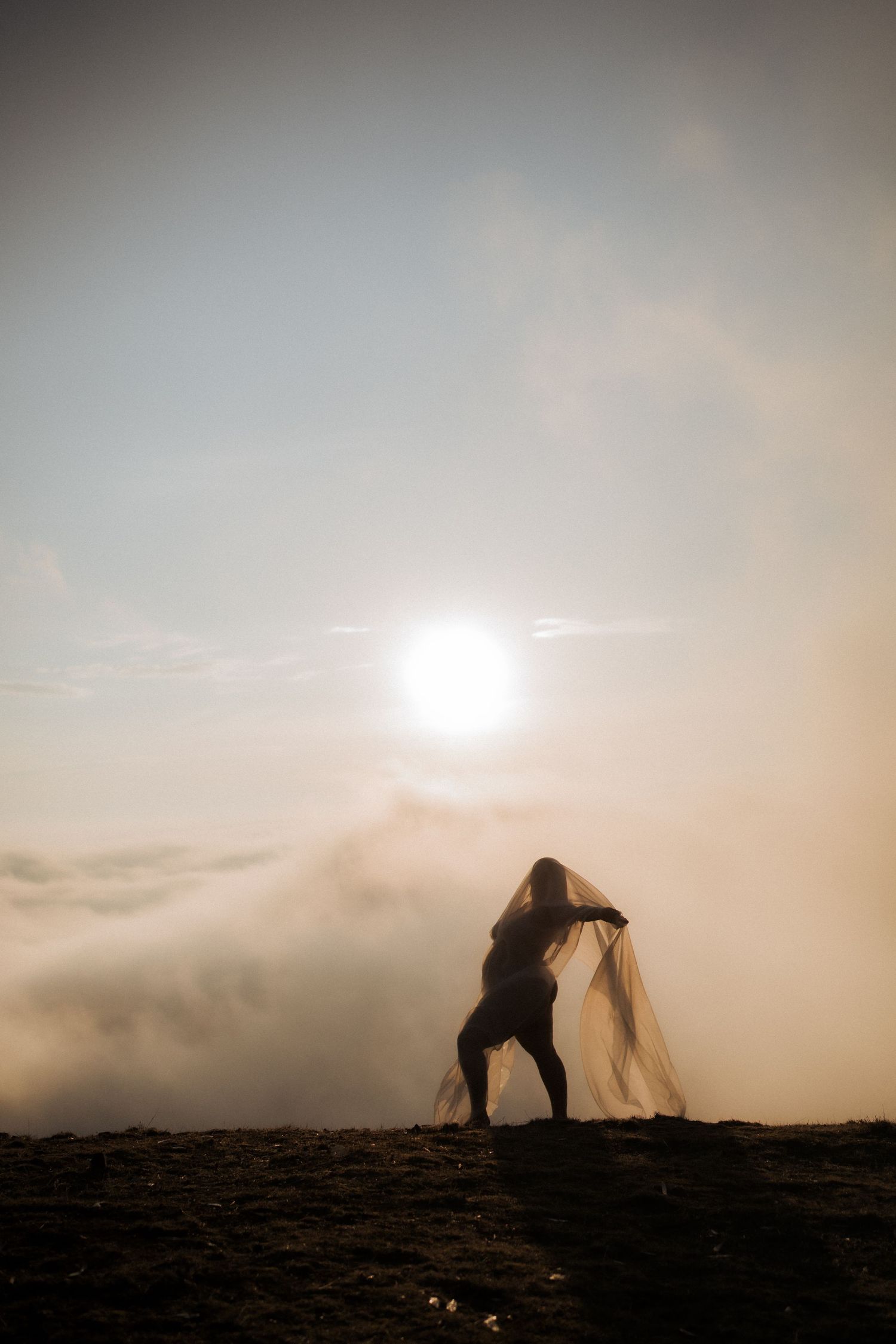 Silhouetted couple dancing together on a hilltop during sunset with dramatic misty skies and a glowing sun.