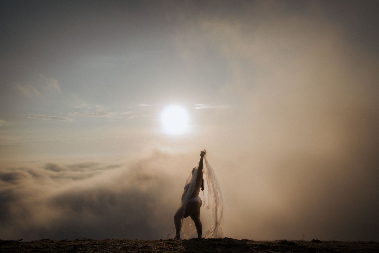 A silhouetted figure stands on a mountain peak at sunset with fog rolling through the valley below.
