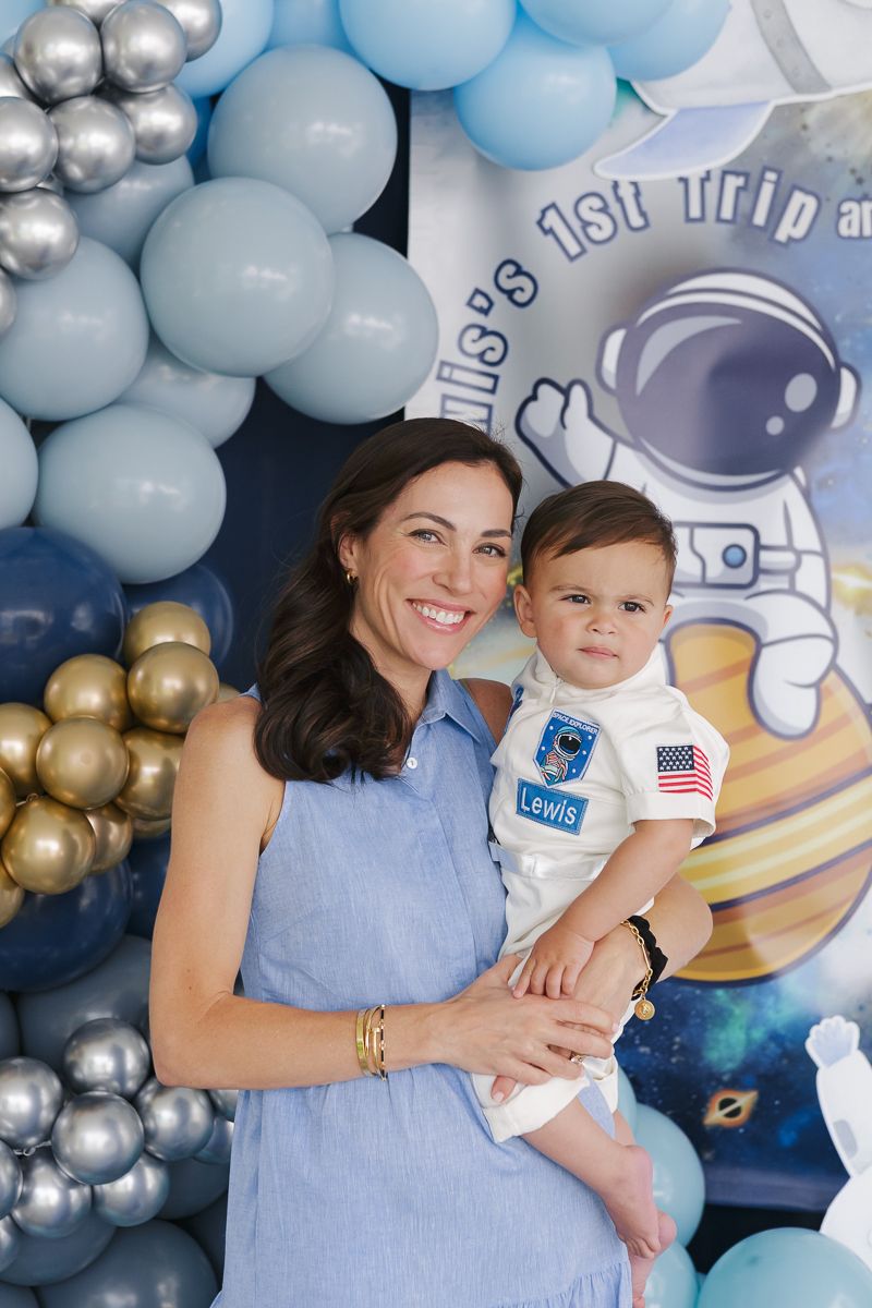 Mother and son share a joyful embrace, surrounded by vibrant balloon decor at his first birthday celebration.