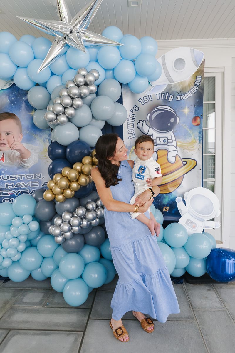 Tender moment—mom and baby boy pose in front of colorful balloon decorations at his space-themed first birthday party in Manhasset.