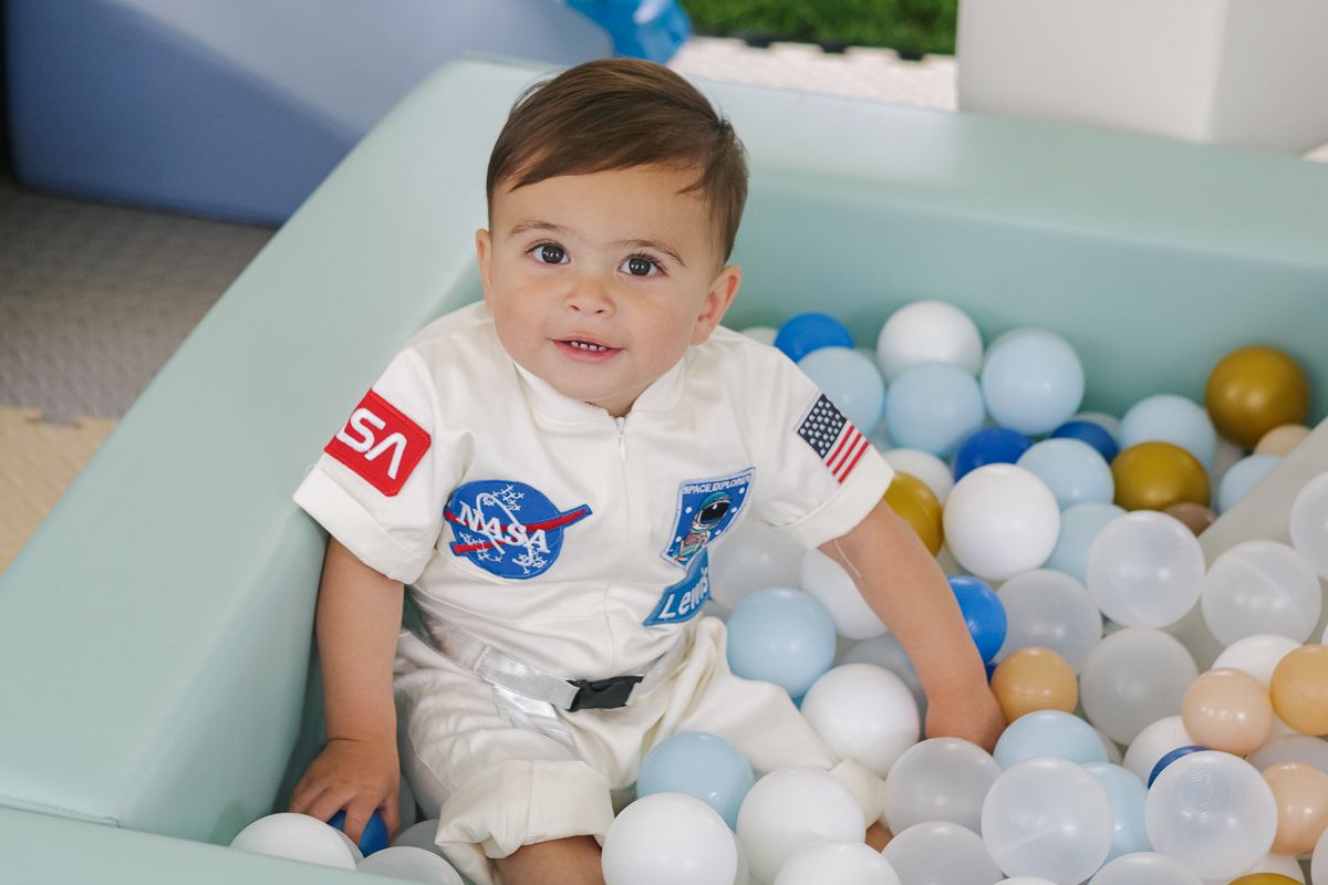 Two hands reaching for colorful balls—birthday boy in his astronaut costume enjoying playful moments by NYC Manhasset Photographer Paula B