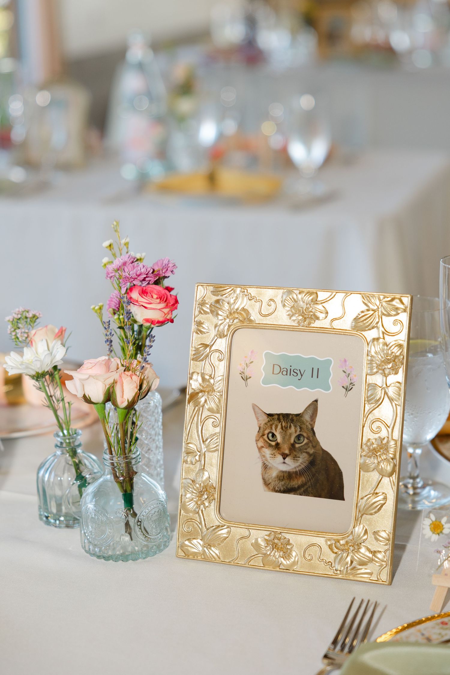 A framed portrait of a black dog named Leila in an ornate gold frame sits on an elegant table setting with champagne glasses.