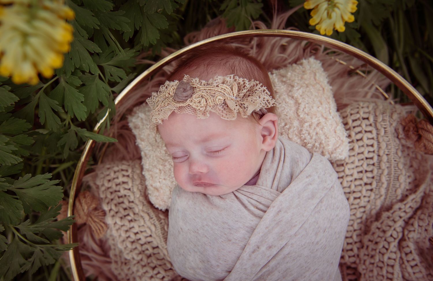 Sleeping newborn swaddled in white fabric resting in knitted blanket with lace headpiece.