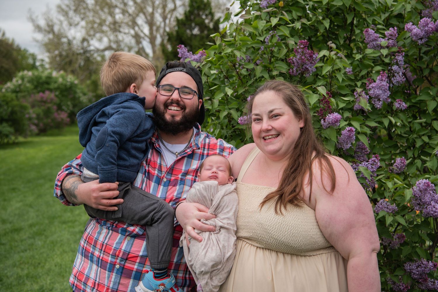 A happy family poses together in front of blooming purple lilac bushes in a spring garden.