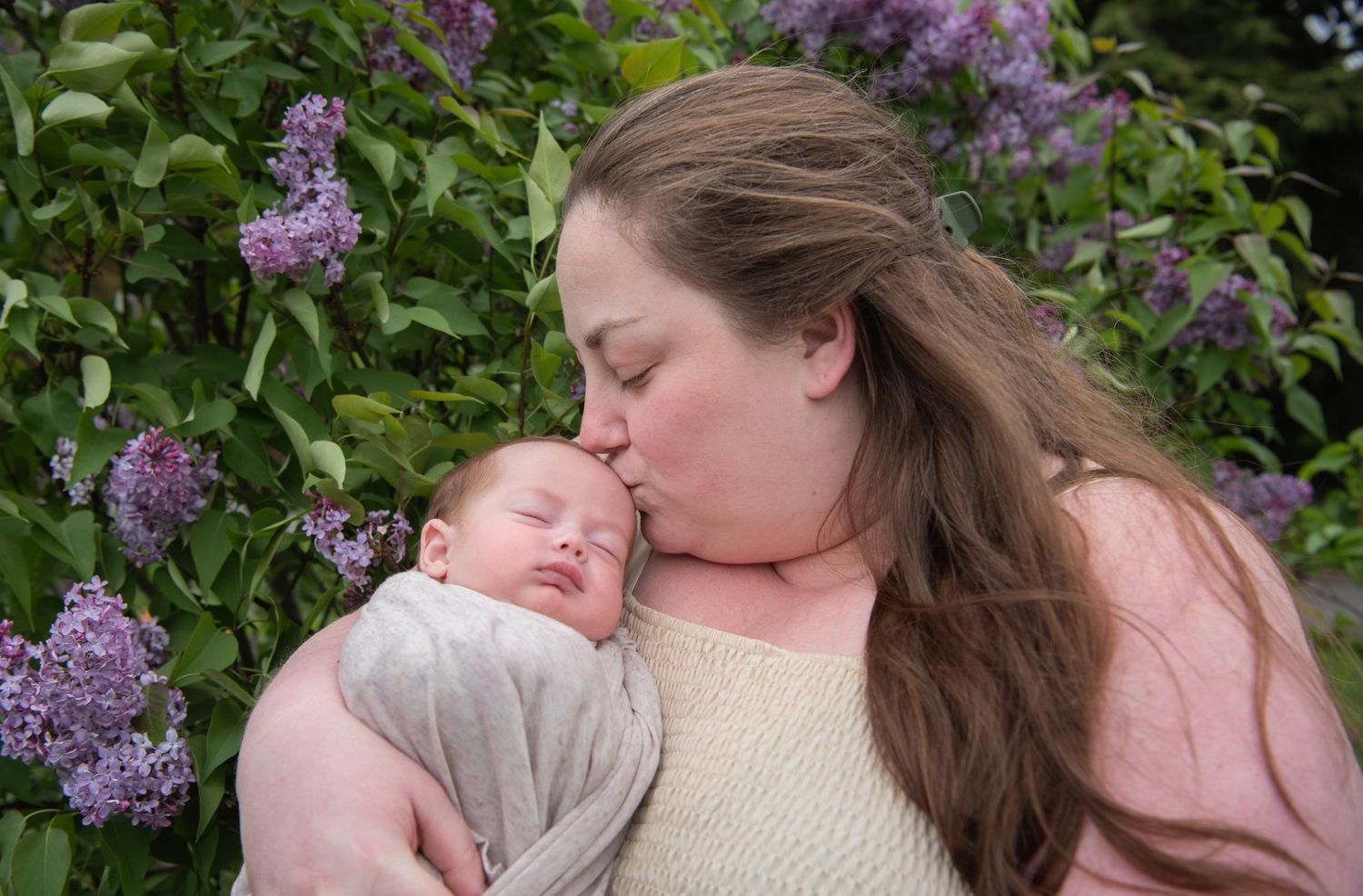 A tender moment captured outdoors with spring lilacs blooming in the background.