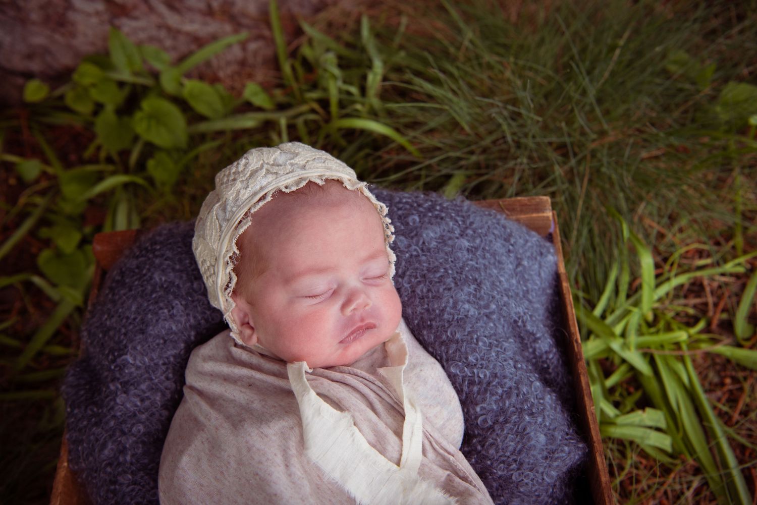 Panoramic collage of a sleeping newborn baby swaddled in white fabric against a dark backdrop and foliage.