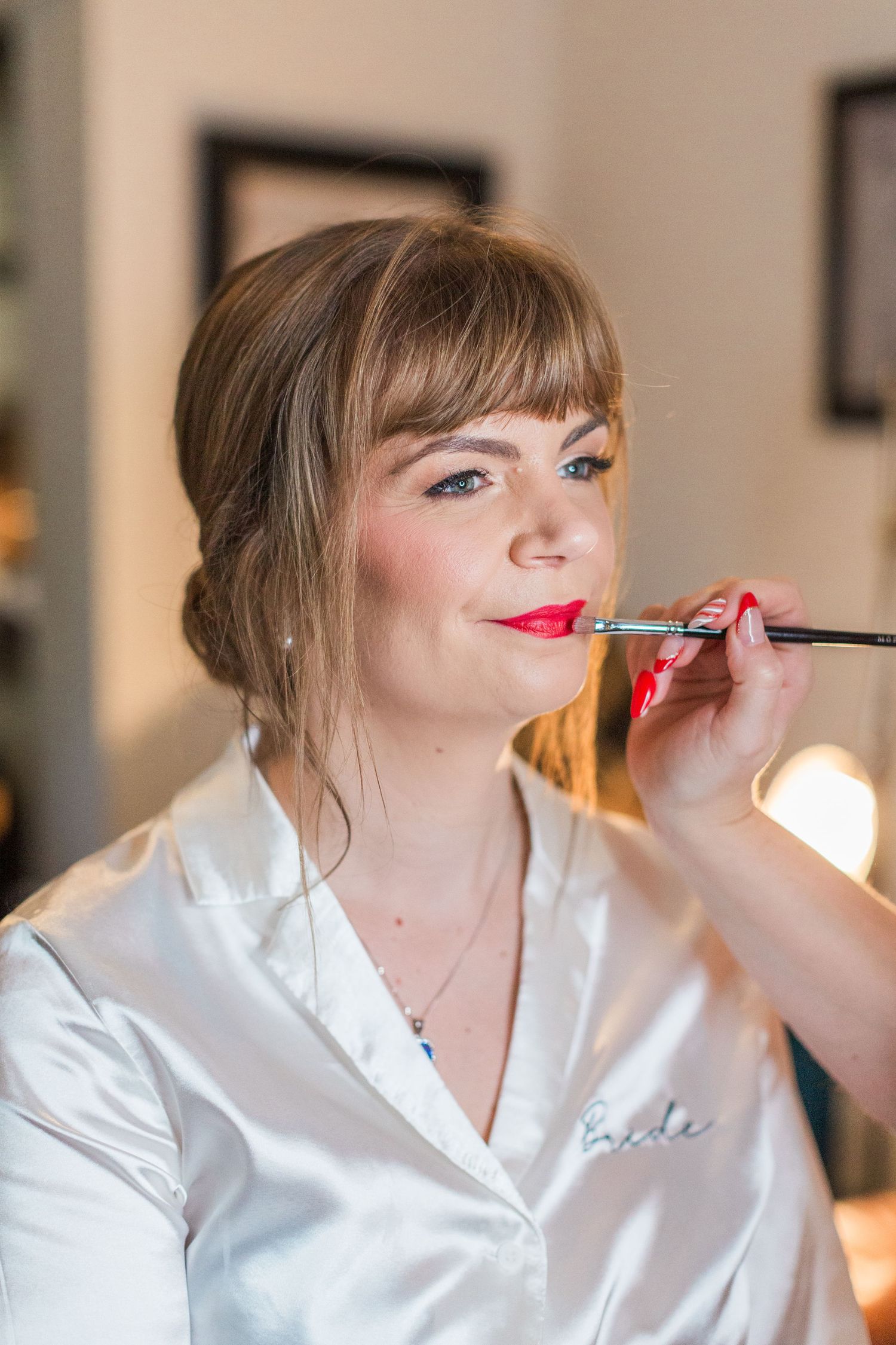 Professional makeup artist applying bright red lipstick to bride in white robe wedding at Deer Park Hall Cotswolds
