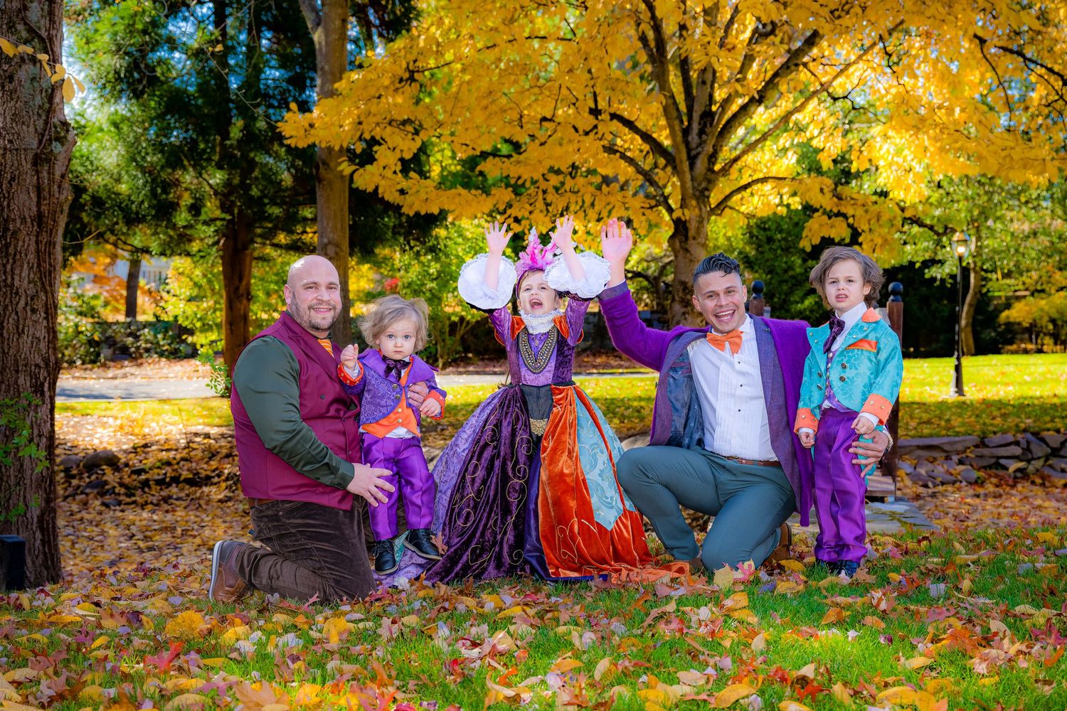 A group wearing purple and autumn colors sits together on fallen leaves beneath a vibrant yellow maple tree in a park.