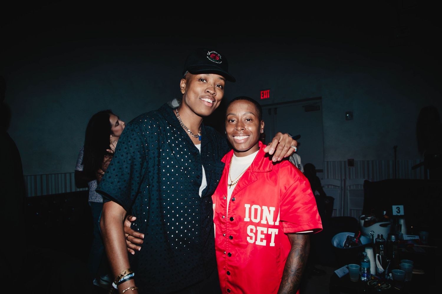 Two people pose together at a dark indoor event venue wearing polka dot and red outfits.