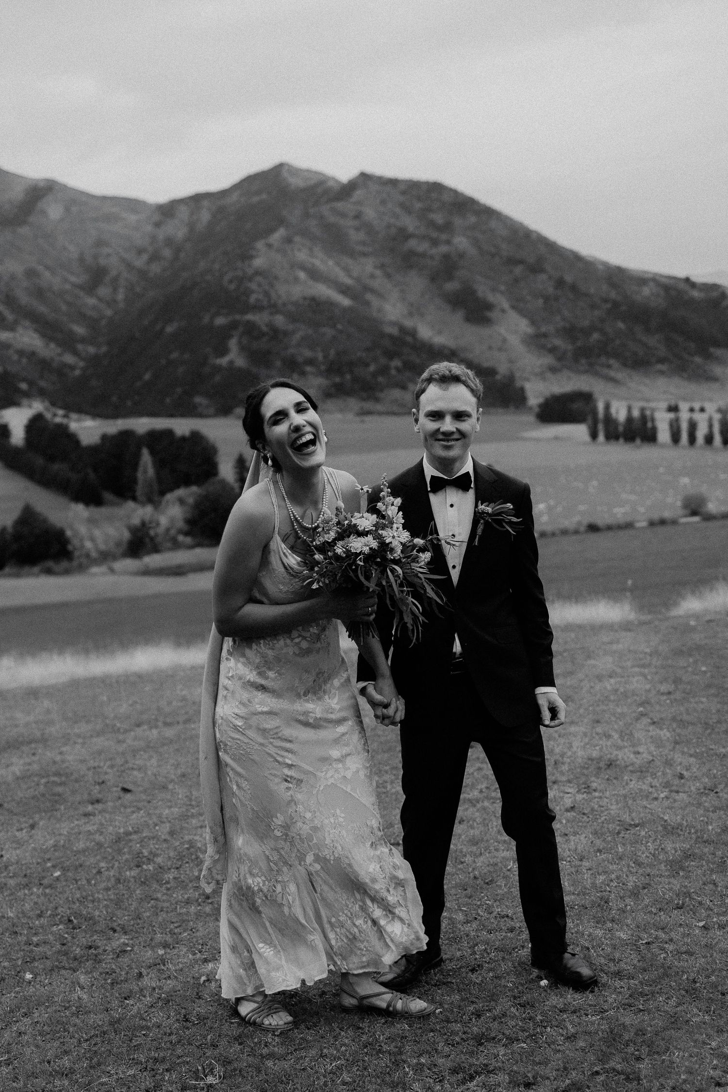 A joyful couple shares a candid moment together against a mountainous landscape during their black and white wedding.
