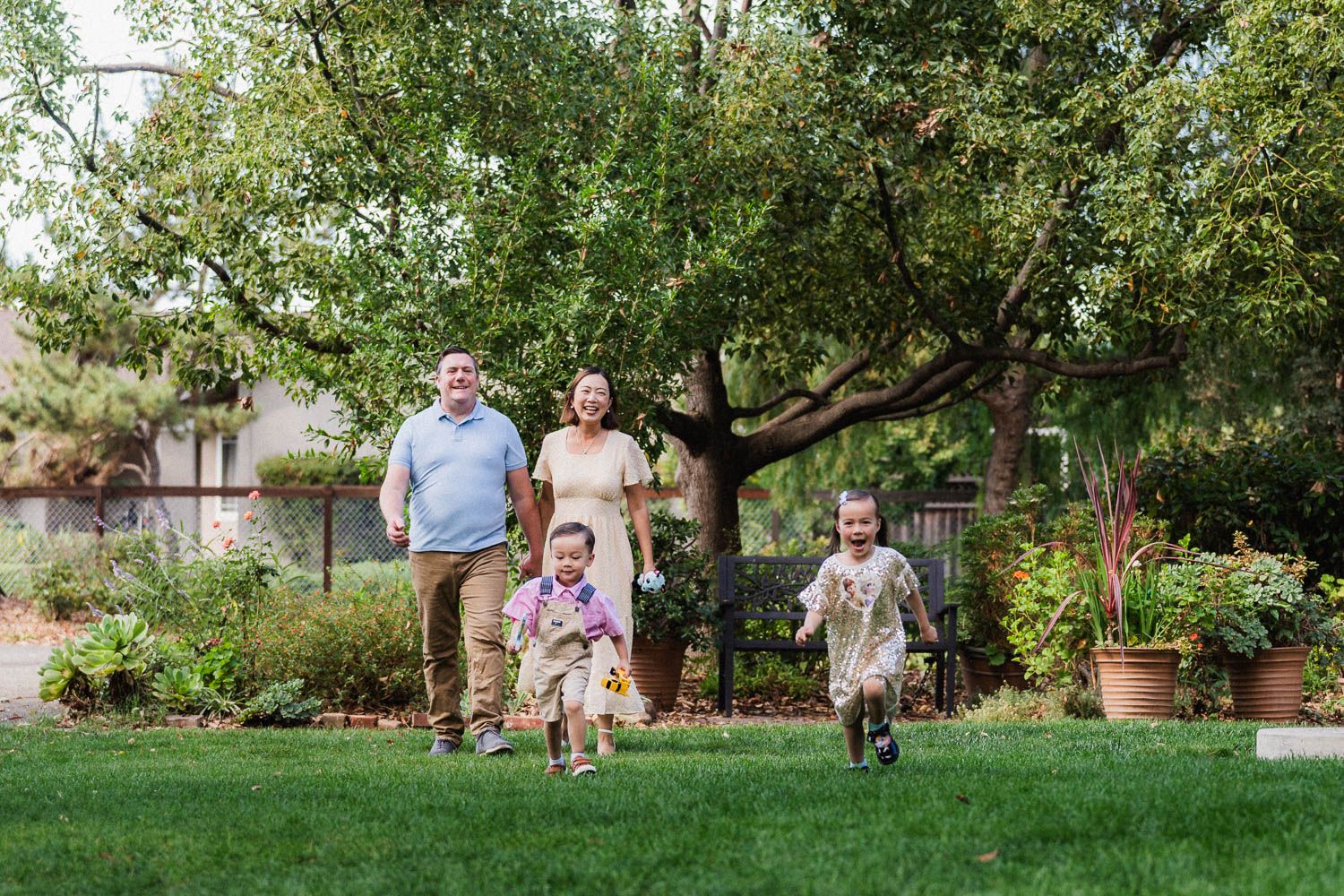 Family enjoying a sunny day outdoors walking through a lush garden setting with trees and greenery.