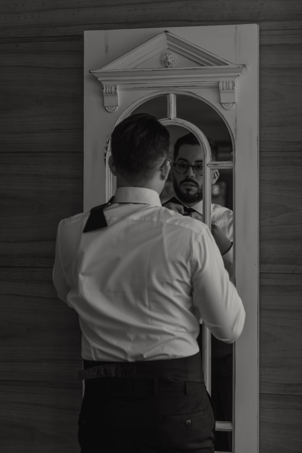 Black and white photo showing a back view of someone looking in an ornate mirror with a decorative arch frame.