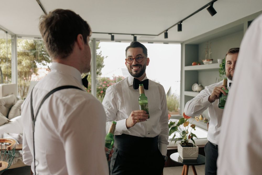 Wedding party members in suspenders and white shirts share drinks and conversation during a celebration.
