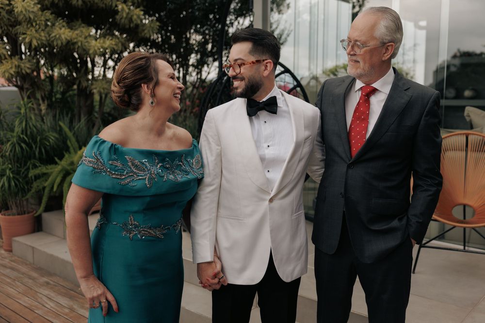 People in semi-formal attire share a group photo and candid moments outdoors next to a white building.
