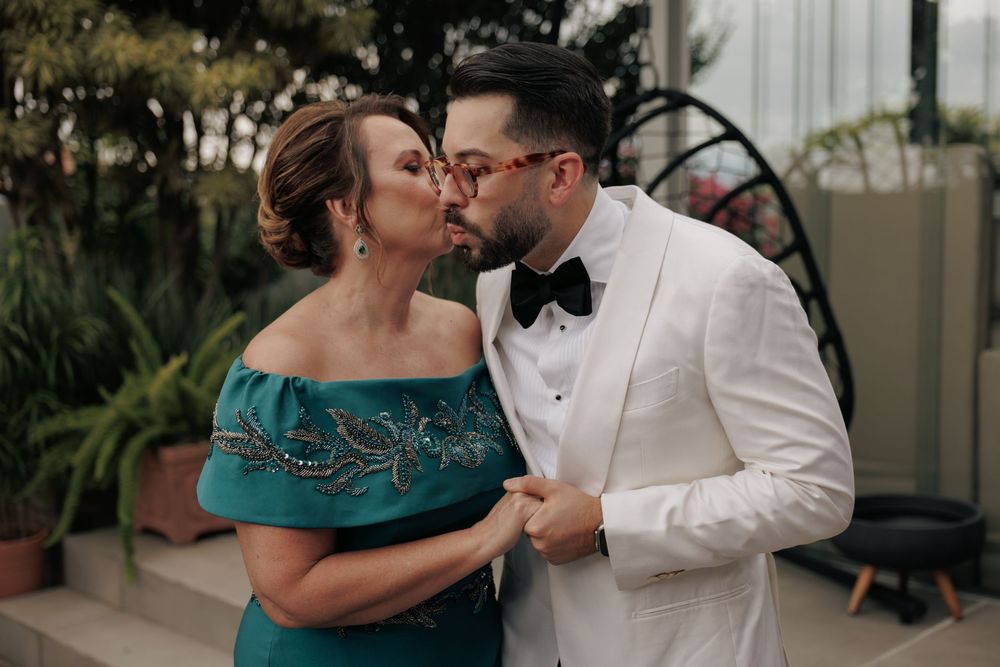Two people sharing an intimate moment at an outdoor venue, with one wearing a white tuxedo and the other in a teal gown.