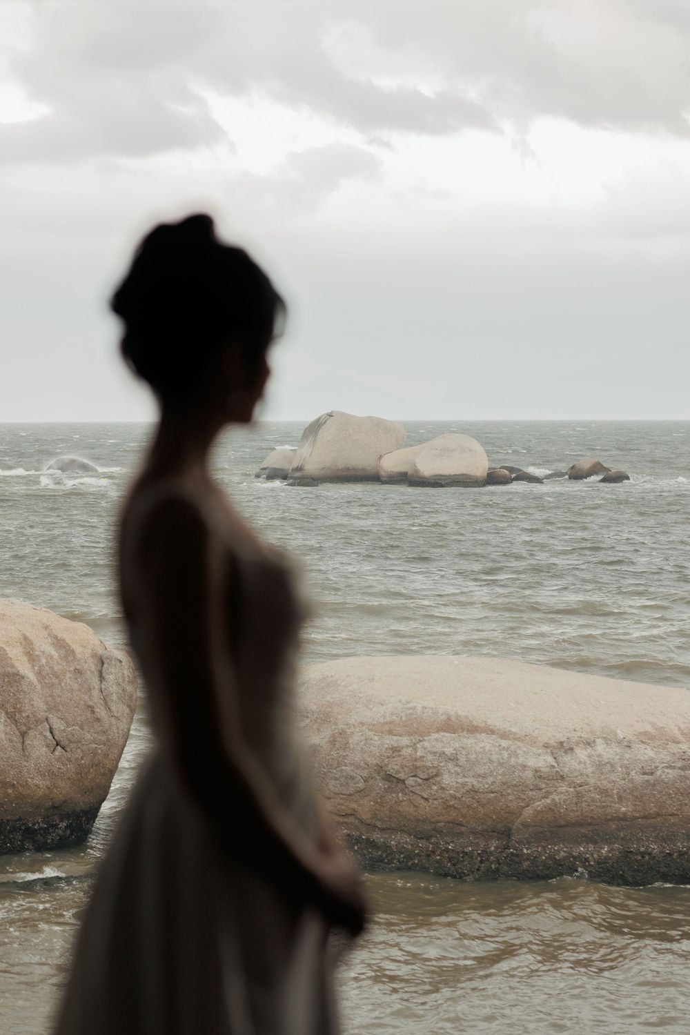 Silhouetted figure looks out over rocky ocean coastline against moody cloudy sky.