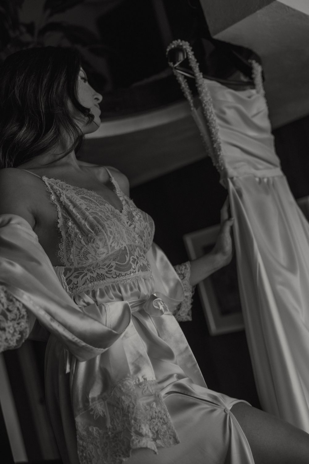 Black and white bridal boudoir photo showing a delicate lace robe with a wedding dress hanging in the background.