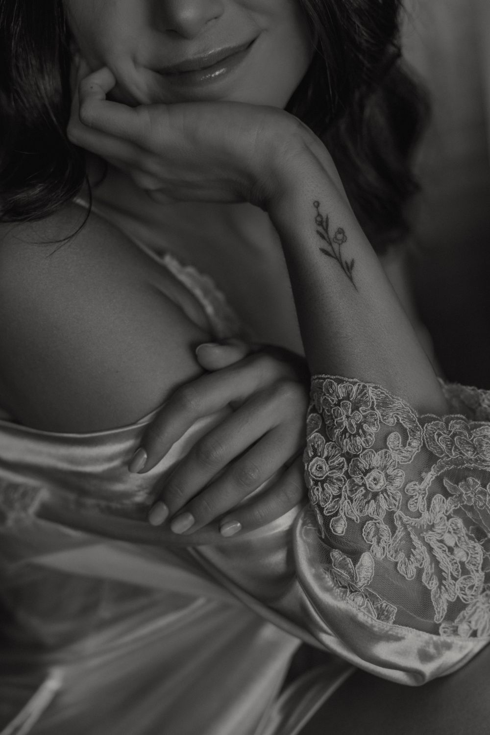 Black and white portrait showing delicate lace lingerie detail and a small floral tattoo on an arm in soft lighting.
