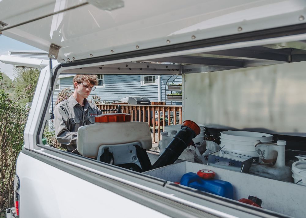 A Modern Pest Control tech checks equipment and supplies inside the open compartment of a white camping van or recreational vehicle.