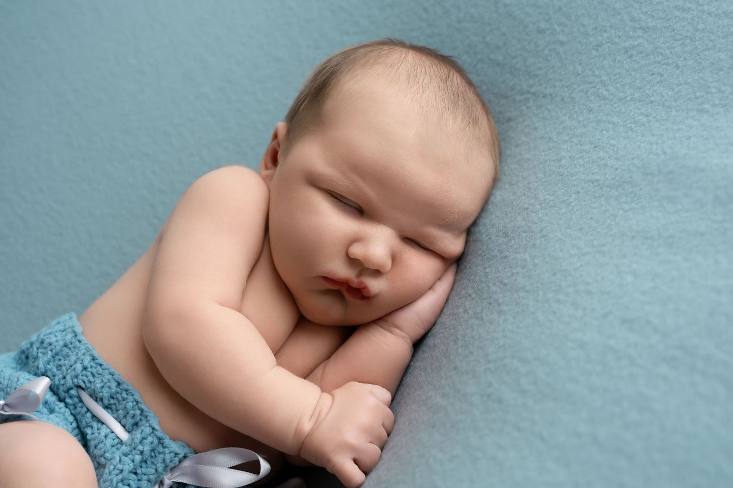 Sleeping newborn baby in blue outfit on blue background.