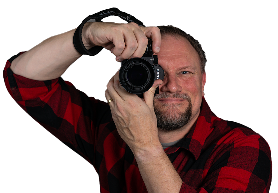 Photographer holding a camera against white background wearing red plaid shirt.