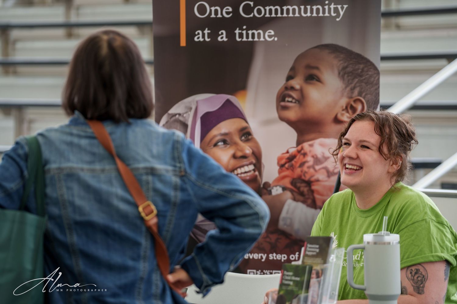 Community event booth with promotional banner and staff members interacting with visitors.