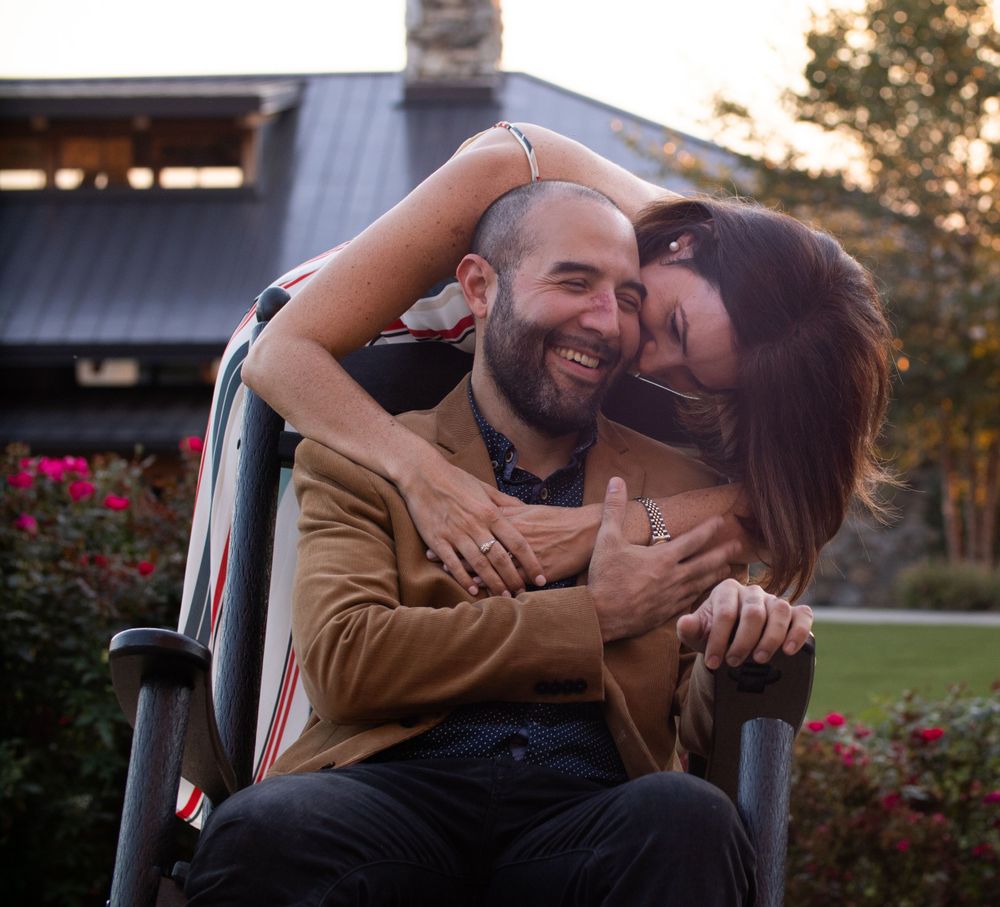 Couple sharing an intimate moment while sitting in wheelchair outdoors at sunset.