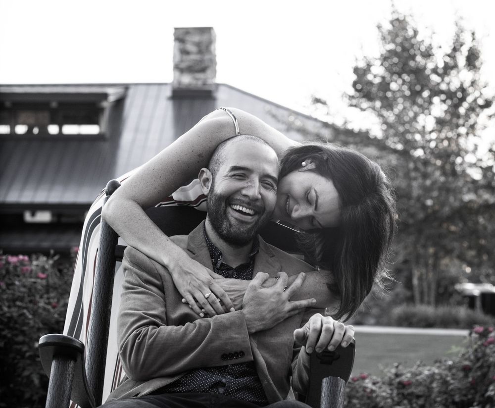 Black and white portrait of couple embracing in wheelchair with building in background.