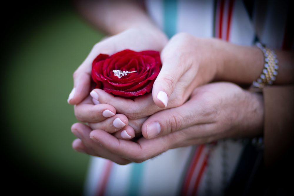Close-up of hands holding a red rose with engagement ring.