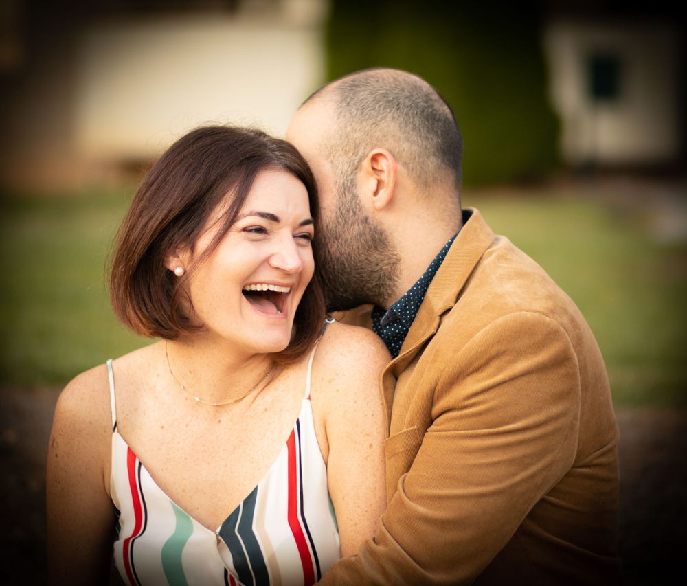 A couple shares an intimate laughing moment outdoors.