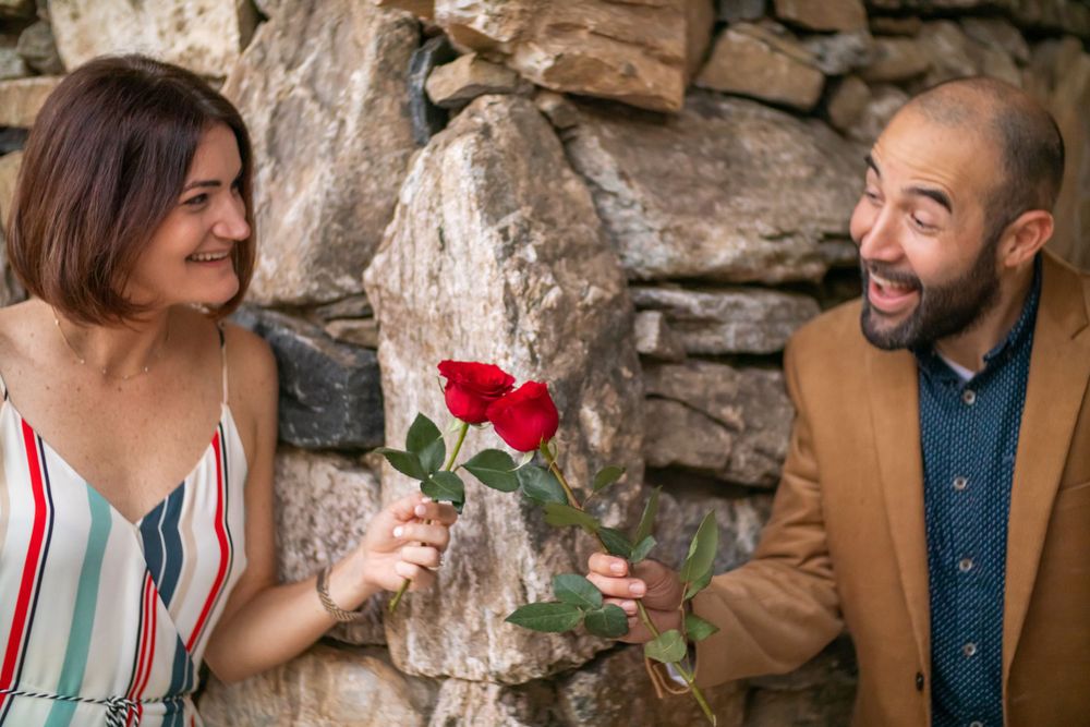 A couple sharing a romantic moment with a red rose against a stone wall backdrop.