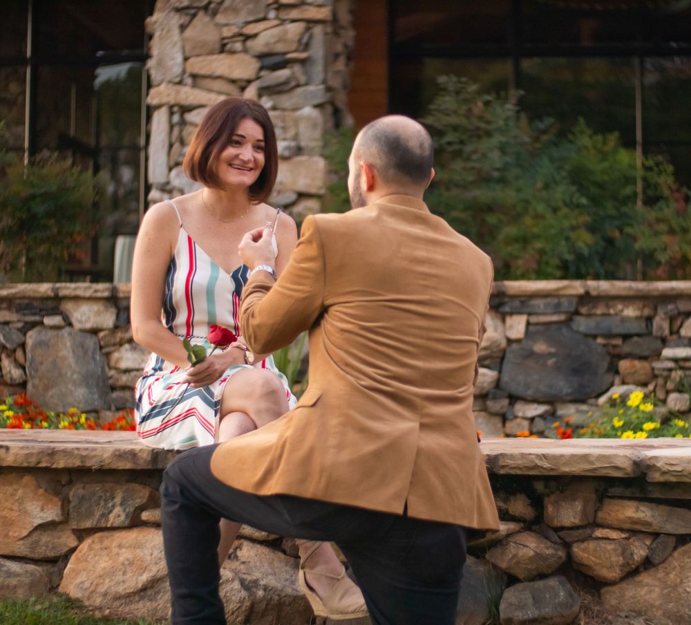 A romantic scene unfolds on a stone wall bench near a rustic building.