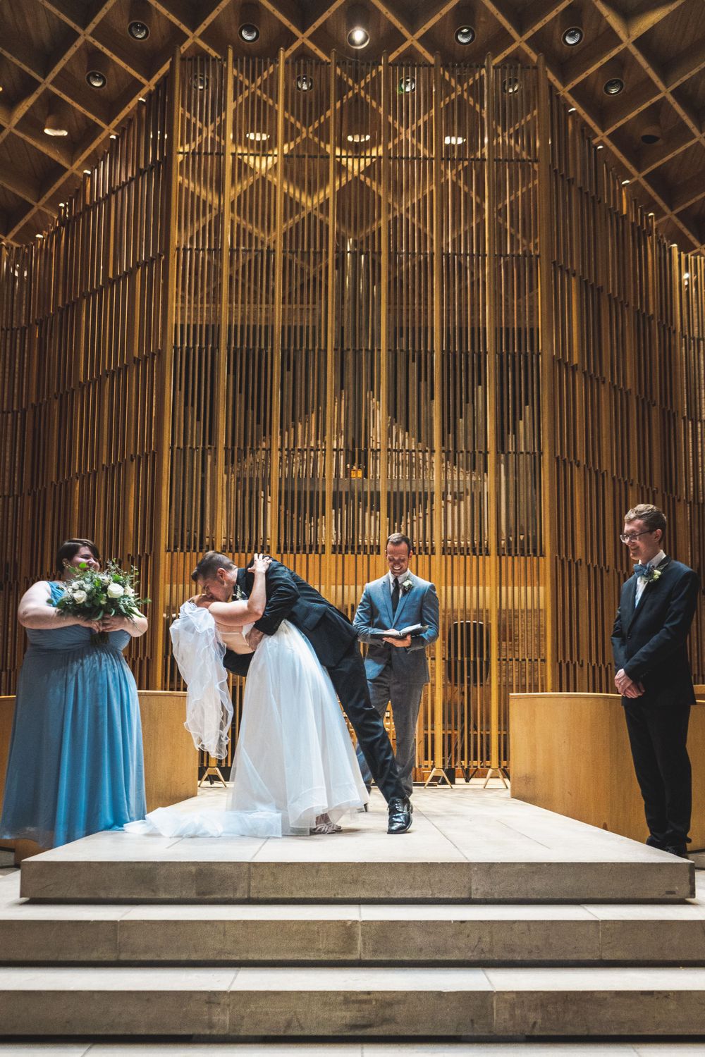 A wedding ceremony in a modern church with dramatic organ pipes creating an architectural backdrop.