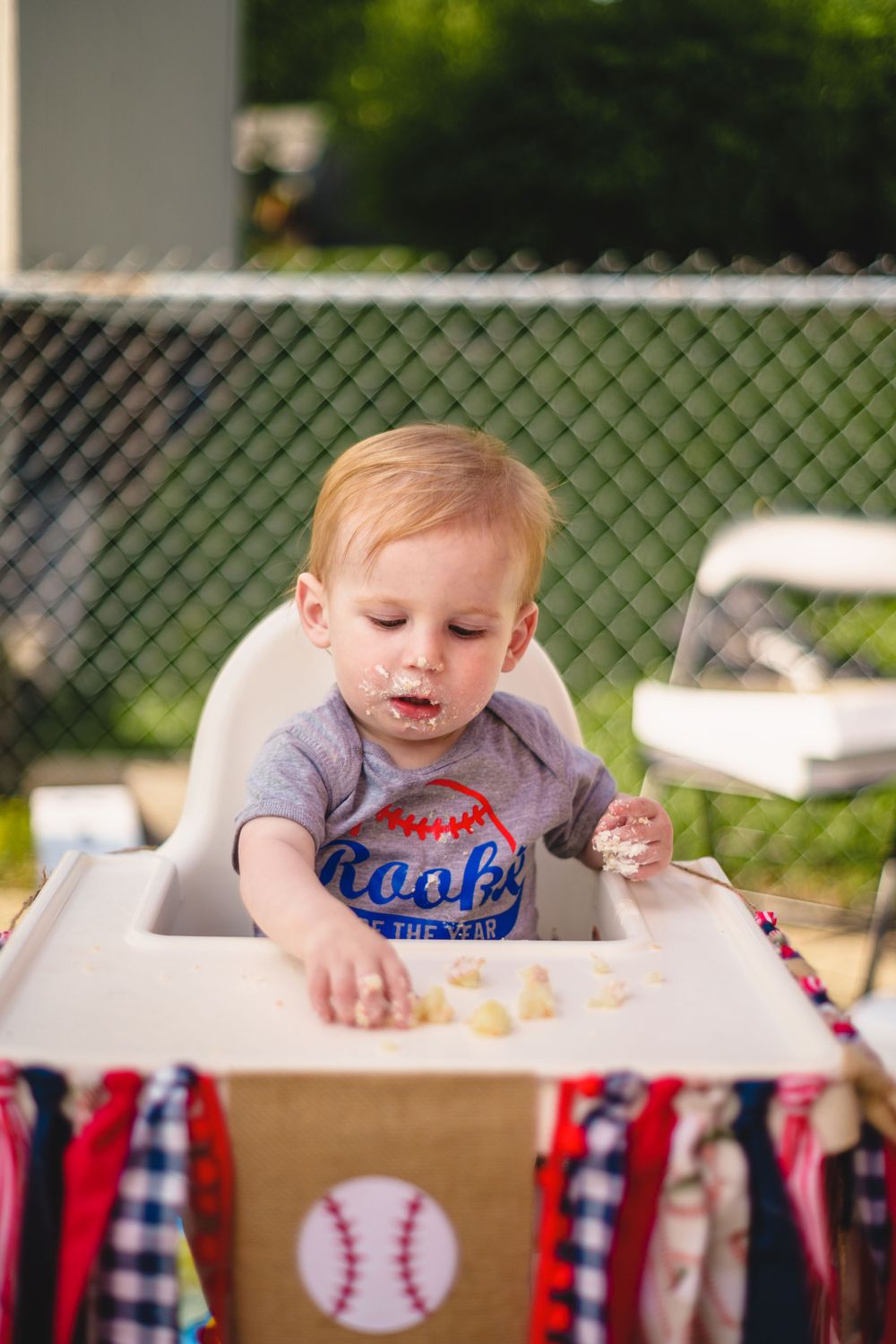 Baby in high chair with baseball themed decorations enjoying a meal time celebration.