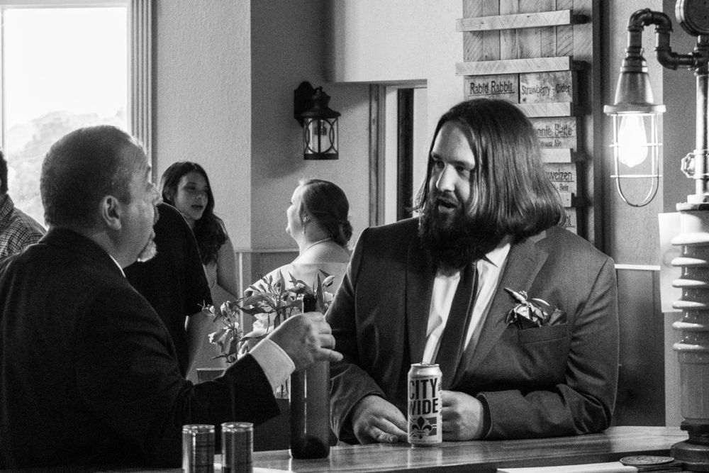 A casual conversation between the groom and his father-in-law at a bar captured in black and white photography.