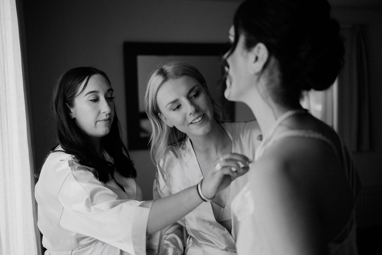 A black and white photo showing three women getting ready in white robes during a special event preparation.