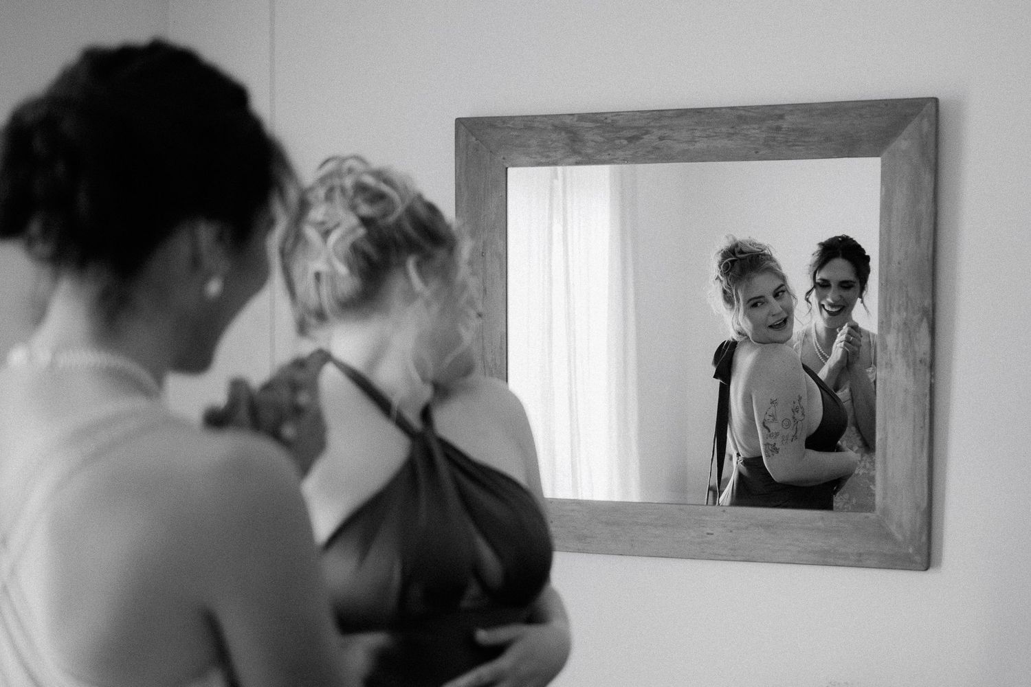 Two people looking at themselves in a framed mirror showing their reflection in black and white photography.
